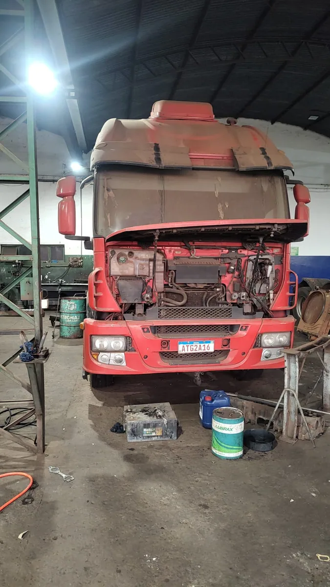 Caminhão vermelho com a dianteira desmontada dentro da oficina